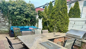 En uteplats med ett bord och stolar i granit, en grill och en blå soffa.