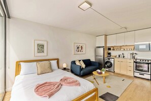 A modern bedroom with a bed, bedside table, and a sofa. There is a kitchen area with a washing machine and an oven. - High Rise 9th Floor City Views Free Pkg, Gym (Salt Lake City)