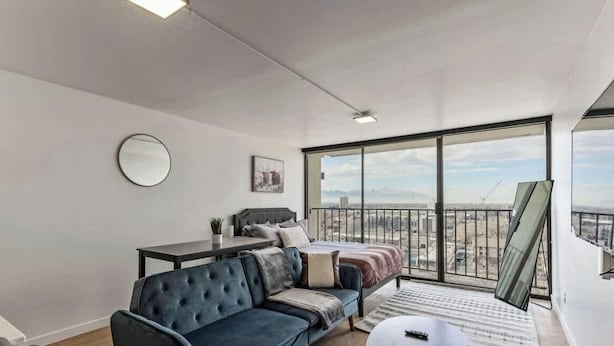 Eine moderne Wohnung mit großem Balkon, einer Couch, einem Bett und einem Schreibtisch.