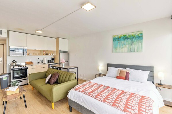 A modern hotel room with a kitchenette, a green sofa, a large bed with a patterned blanket, and a painting on the wall. - Mountain View 9th Floor City Views Free Pkg, Gym (Salt Lake City)