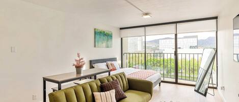 Una sala moderna con un sofá, una mesa de comedor y un amplio ventanal con vistas a edificios y montañas.