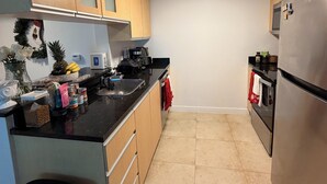 Een kleine keuken met houten kastjes, een roestvrijstalen koelkast, een koffiezetapparaat en een prullenbak.