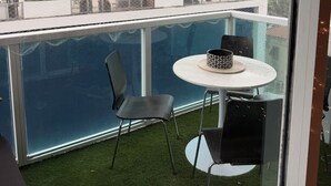 Een balkon met glazen hekwerk, een ronde tafel met stoelen en hangende lampen.