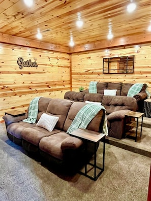 Ein gemütlicher Raum mit Holzwandverkleidung, einem 'Cather'-Schild, zwei braunen Sofas mit karierten Decken und einem kleinen Tisch.