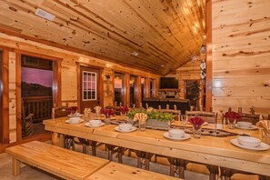 Ein Holzhütten-Innenraum mit einem langen Esstisch, der für eine Mahlzeit gedeckt ist, Holzwänden und einem Kamin.