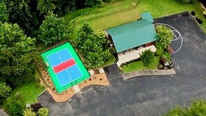 Vue aérienne d’une propriété comprenant un court de tennis, un bâtiment doté d’un toit végétalisé et un espace de stationnement.