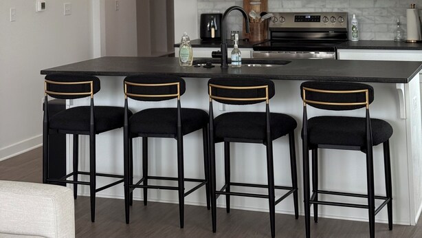 A modern kitchen with white cabinets, a central island with bar stools, a microwave, and a stove.