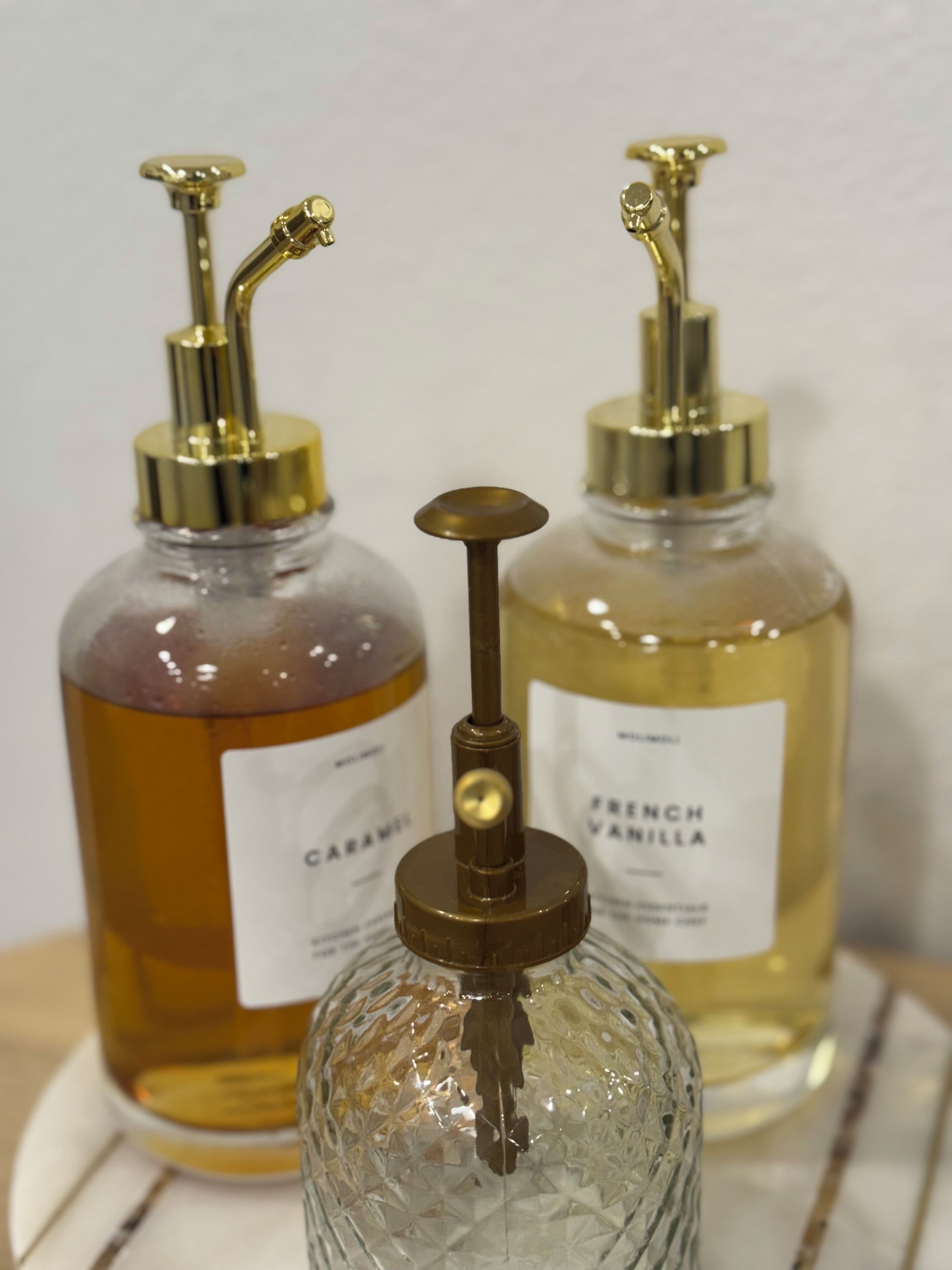 Twee parfumflesjes met pompen, waarvan één 'CARAMEL' en de andere 'FRENCH VANILLA' is, op een witte ondergrond.