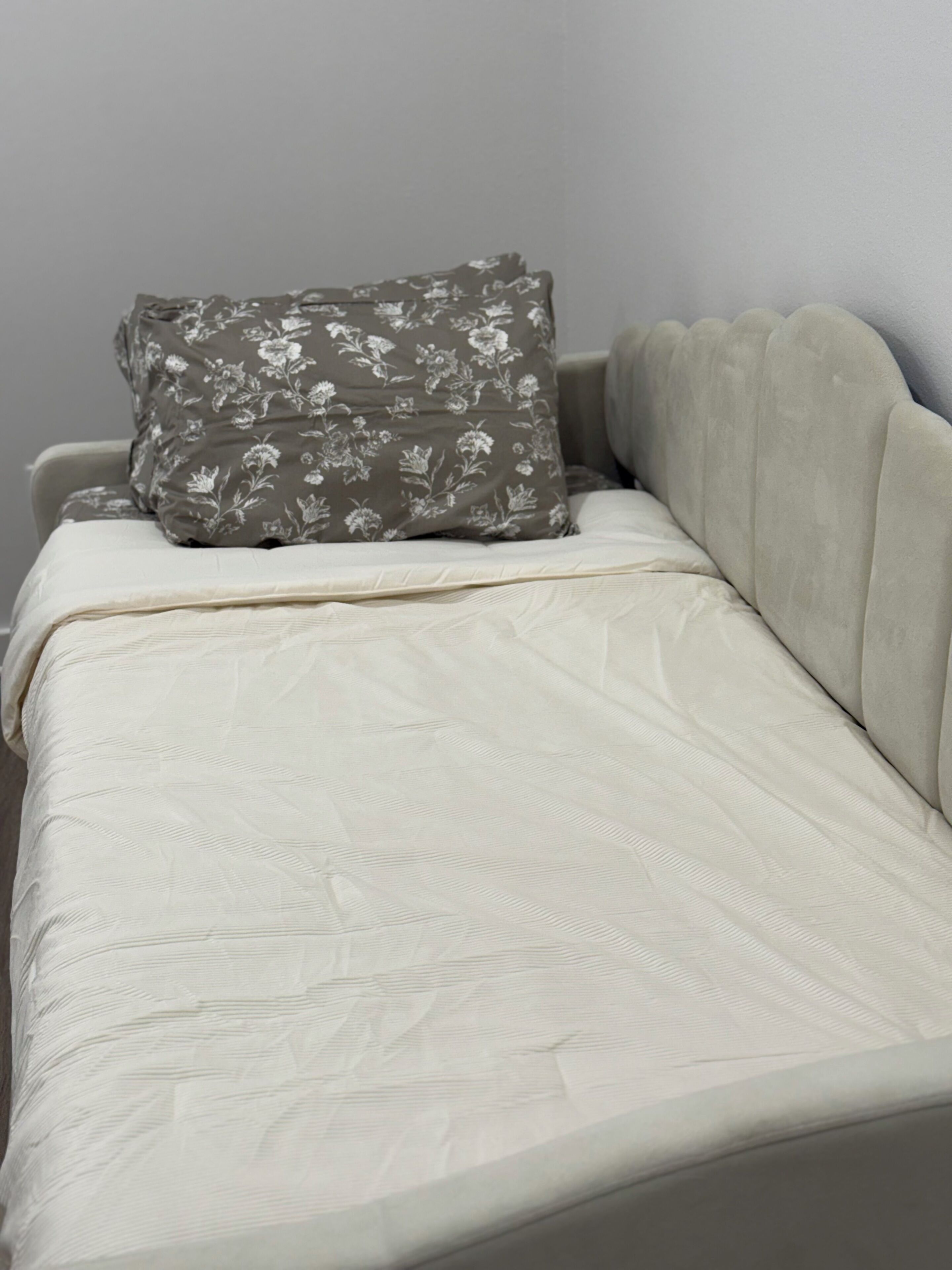 A bed with a floral pillow and a textured blanket.