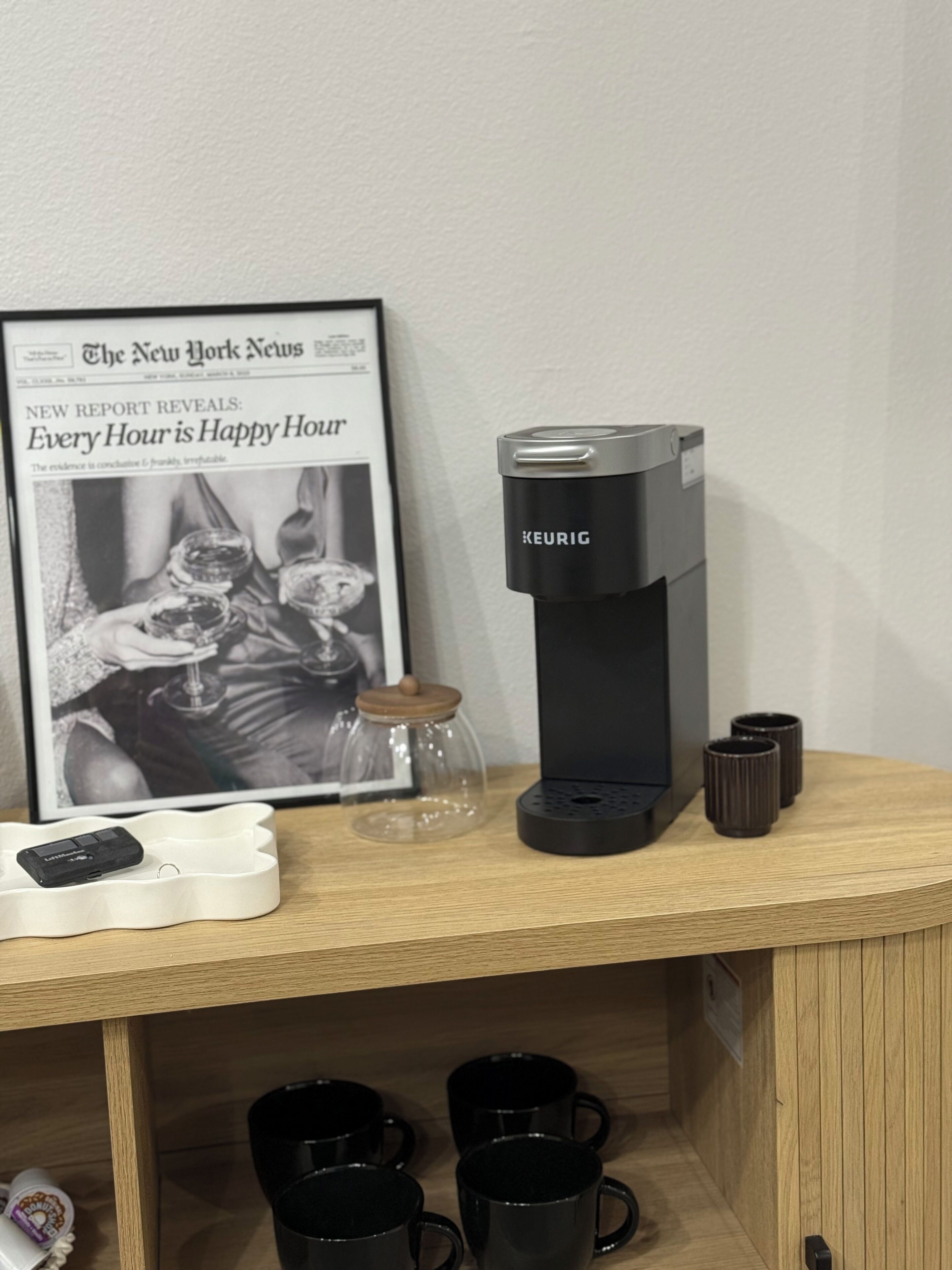 A coffee maker, a framed newspaper, and a car charger on a wooden table.