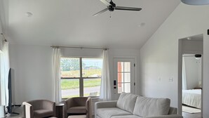 A modern living room with a sofa, chairs, a dining table, and a ceiling fan.