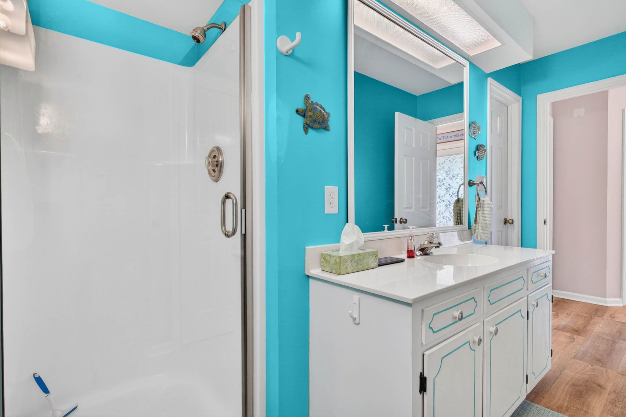 A bathroom with a white door, a large mirror, a white sink, and a turquoise accent wall.