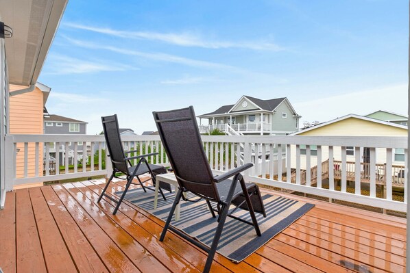 A wooden deck with two black chairs and a striped rug.