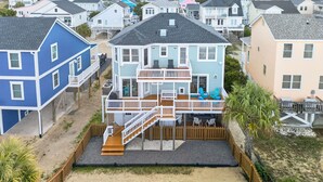 Una casa frente al mar de varios pisos con terraza, asientos al aire libre y vista a la playa.