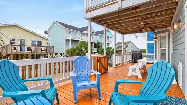 Una terraza de madera con sillas Adirondack azules, un espacio cubierto y vista a casas vecinas.