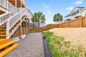 A coastal building with a wooden staircase, a sandy beach, and palm trees. - The Ideal Spot (Holden Beach)