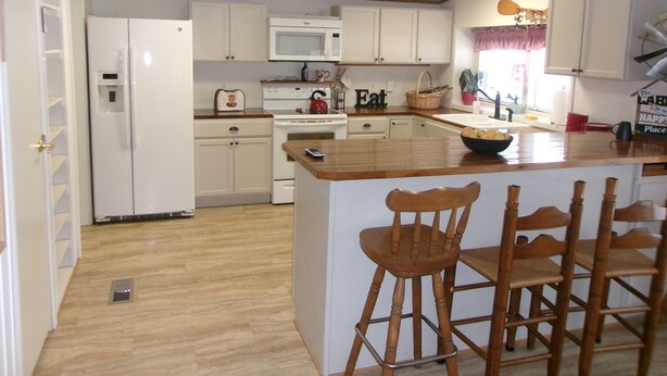 Una cocina con armarios blancos, microondas, estufa, pileta y una isla de madera con taburetes de bar.