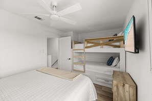 Ein Schlafzimmer mit Etagenbett, Deckenventilator, Fernseher und Nachttisch aus Holz.