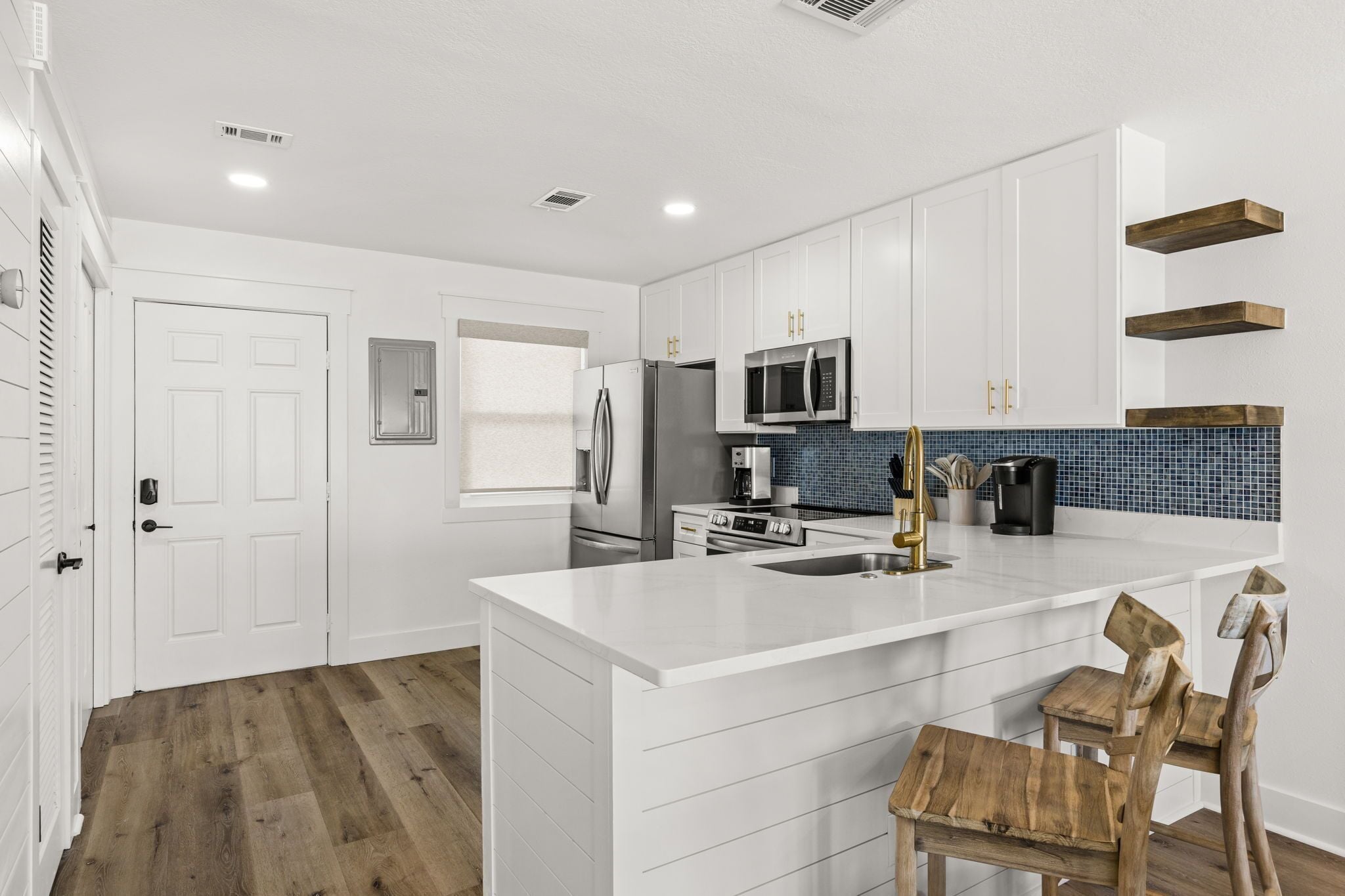 A modern kitchen with white cabinetry, a central island, stainless steel appliances, and a blue-tiled backsplash.