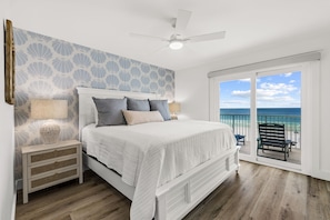 A bedroom with a bed, nightstands, a lamp, a ceiling fan, and a view of the ocean through a sliding glass door. - Brand NEW Luxury Beachfront Paradise ~ Minutes to 30a! (Panama City Beach)