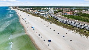 Un hôtel situé sur la côte, composé de plusieurs bâtiments, avec une plage équipée de parasols et offrant une vue dégagée sur l’océan.