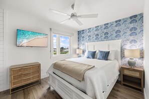 A bedroom with a bed, a ceiling fan, a television, a window, and a wall with a floral pattern. - Brand NEW Luxury Beachfront Paradise ~ Minutes to 30a! (Panama City Beach)