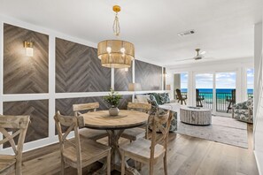 A modern interior with a dining area, a round table, and chairs. There is a view of the ocean through large windows. - Brand NEW Luxury Beachfront Paradise ~ Minutes to 30a! (Panama City Beach)