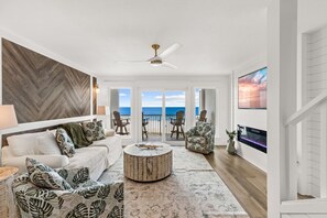 Ein geräumiges Wohnzimmer mit einem weißen Sofa, gemusterten Sesseln, einem runden Couchtisch und einem Fernseher an der Wand.