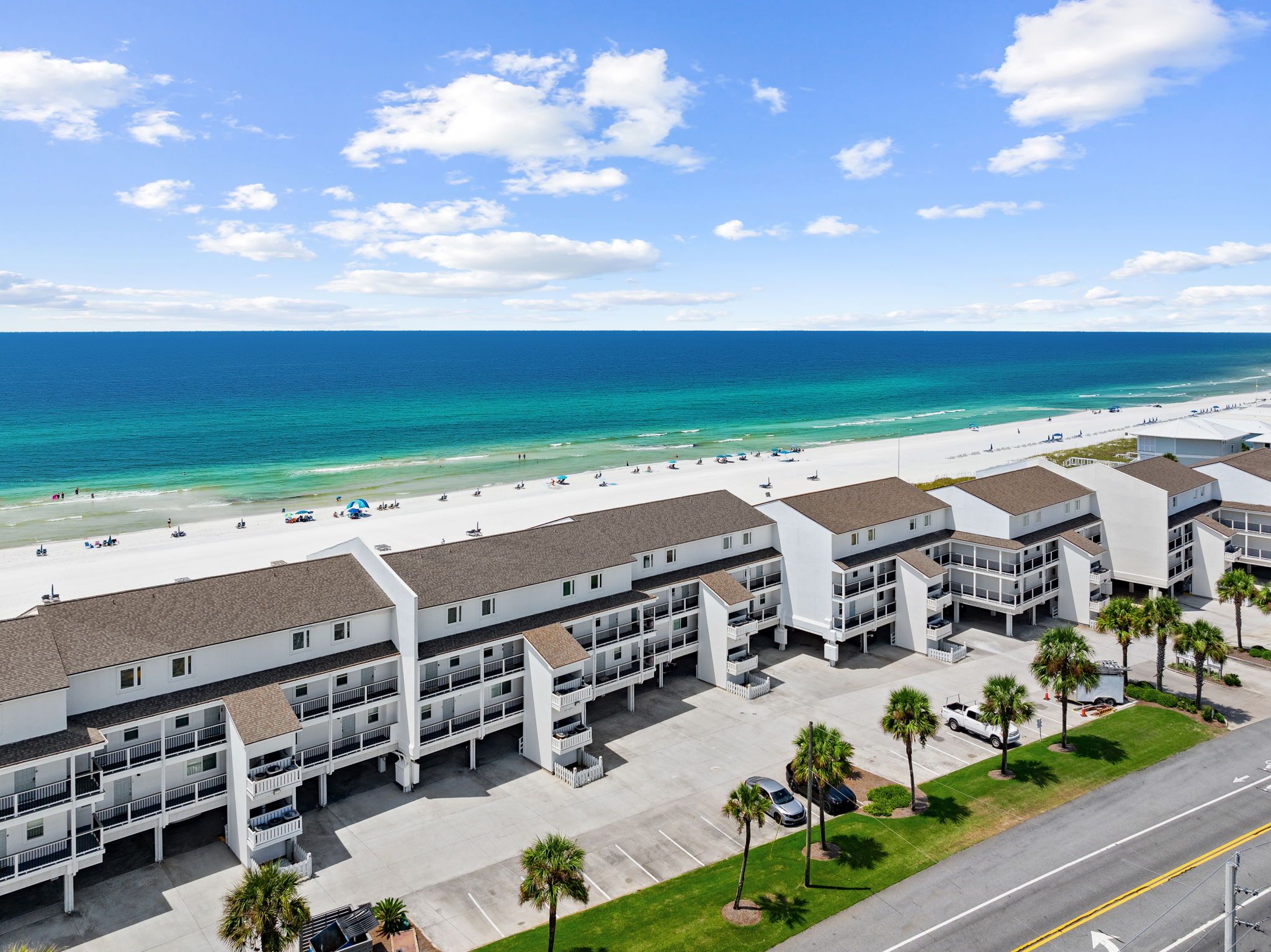 A beachfront hotel with multiple balconies, a parking lot, and a view of the ocean.