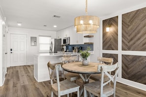 A modern kitchen with white cabinetry, a central island, and a round wooden dining table with chairs. - Brand NEW Luxury Beachfront Paradise ~ Minutes to 30a! (Panama City Beach)