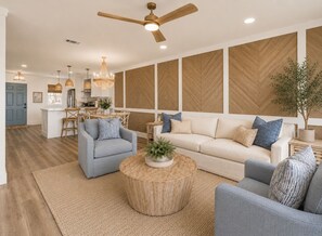 Ein modernes Wohnzimmer mit einer Couch, zwei Sesseln, einem Couchtisch und einem Essbereich mit einer Küche im Hintergrund.