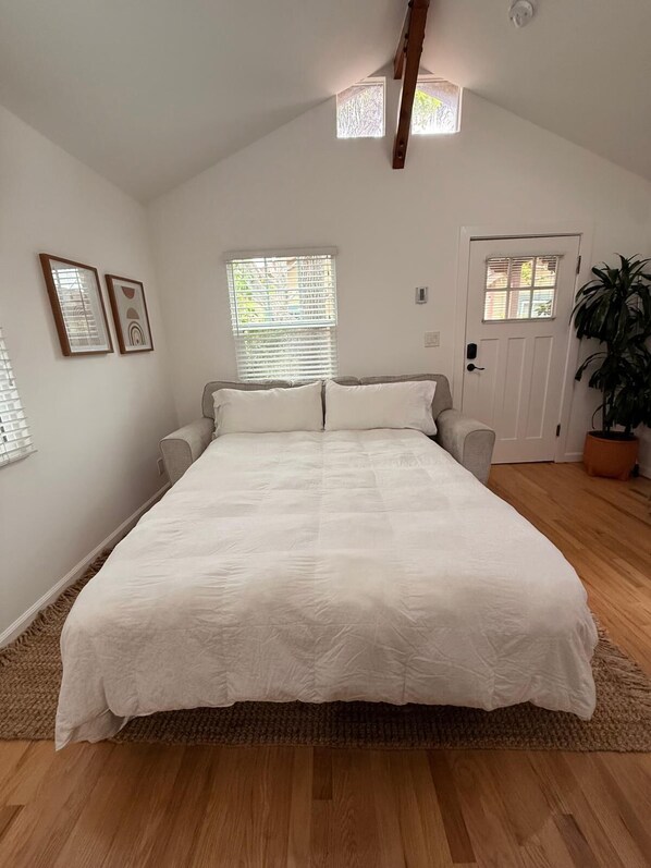 A bedroom with a large bed, a door, a window, and a potted plant.