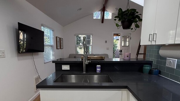A modern kitchen with a black countertop, white cabinets, a stainless steel sink, a built-in oven, and a flat-screen TV mounted on the wall. - Newly renovated, Stylish Studio Beach Bungalow a couple of blocks from the beach (Los Angeles)