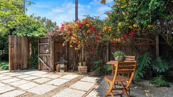 A patio with a wooden table and chairs, surrounded by a garden with flowering plants and a wooden fence.