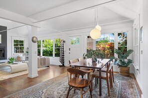 Un salón espacioso con una gran mesa de comedor, asientos cómodos y vistas a un jardín a través de las ventanas.