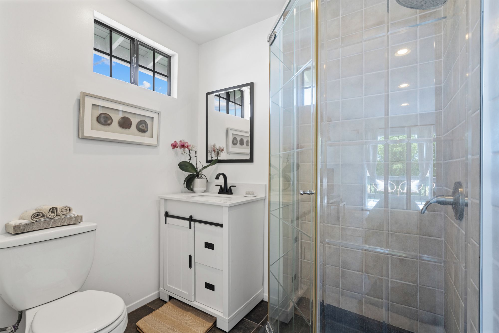 A modern bathroom with a toilet, vanity, and a glass shower enclosure.