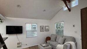 A living room with a grey sofa, a coffee table, a TV, and a wooden floor. - Newly renovated, Stylish Studio Beach Bungalow a couple of blocks from the beach (Los Angeles)