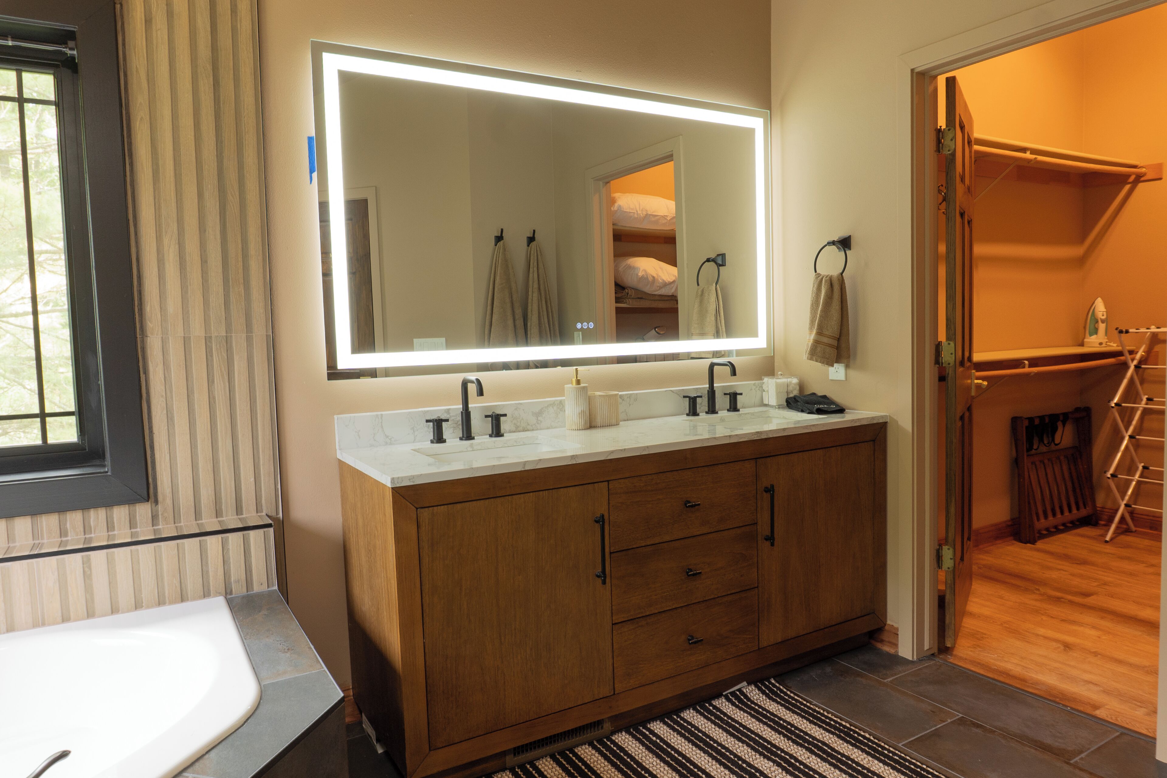 A bathroom with a large mirror, a double sink vanity, and a walk-in closet.