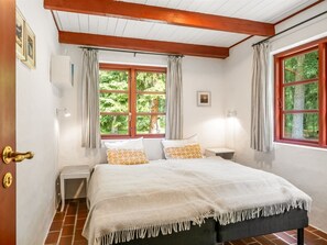 Quarto com cama, duas janelas, mesa de cabeceira e porta com puxador de latão.