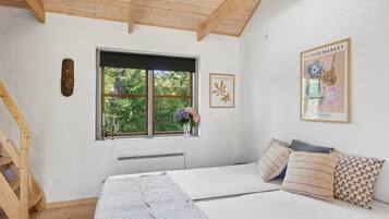 Ein Schlafzimmer mit Holzboden, einem Fenster mit Blick ins Grüne, einem Bett mit gemusterten Textilien und einer Wand mit gerahmten Kunstwerken.