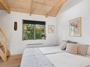 A bedroom with a wooden ceiling, a window with a view of greenery, a bed with patterned bedding, and a wall with framed artwork. - "Thorvor" - 900m from the sea by Interhome (Asnæs)