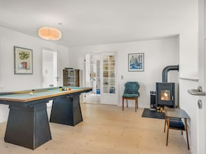 Une pièce avec une table de billard, un fauteuil bleu, une cheminée et une bibliothèque.