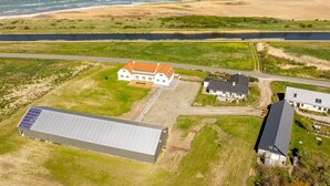 Vue aérienne d’une propriété située sur la côte, comprenant un grand bâtiment, une maison plus petite et un ensemble de panneaux solaires.