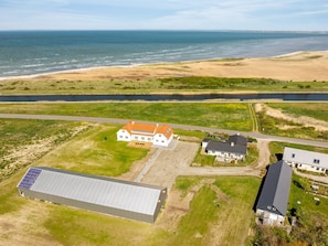 Vue aérienne d’une propriété située sur la côte, comprenant un grand bâtiment, une maison plus petite et un ensemble de panneaux solaires.
