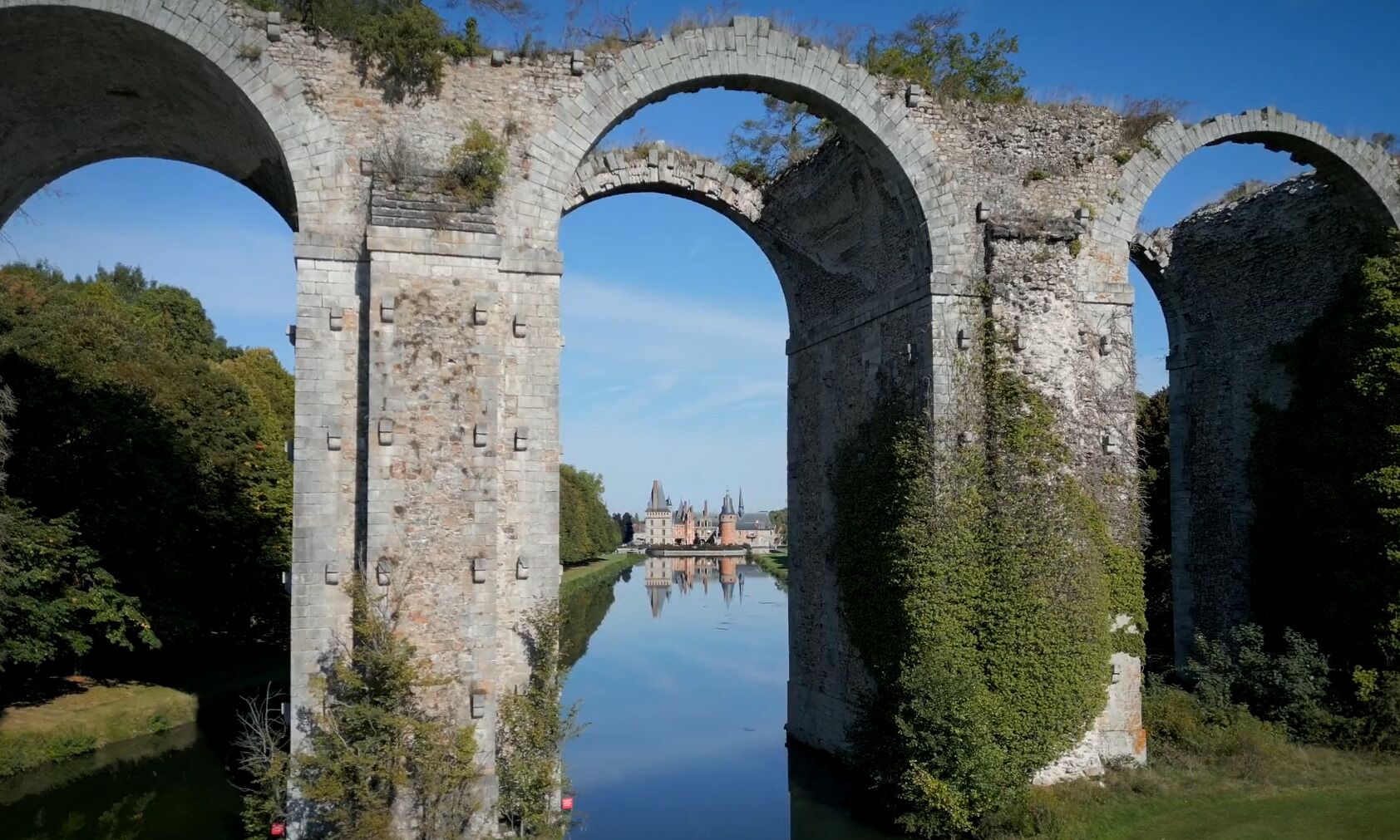 A stone bridge with arches over a calm river, surrounded by greenery.