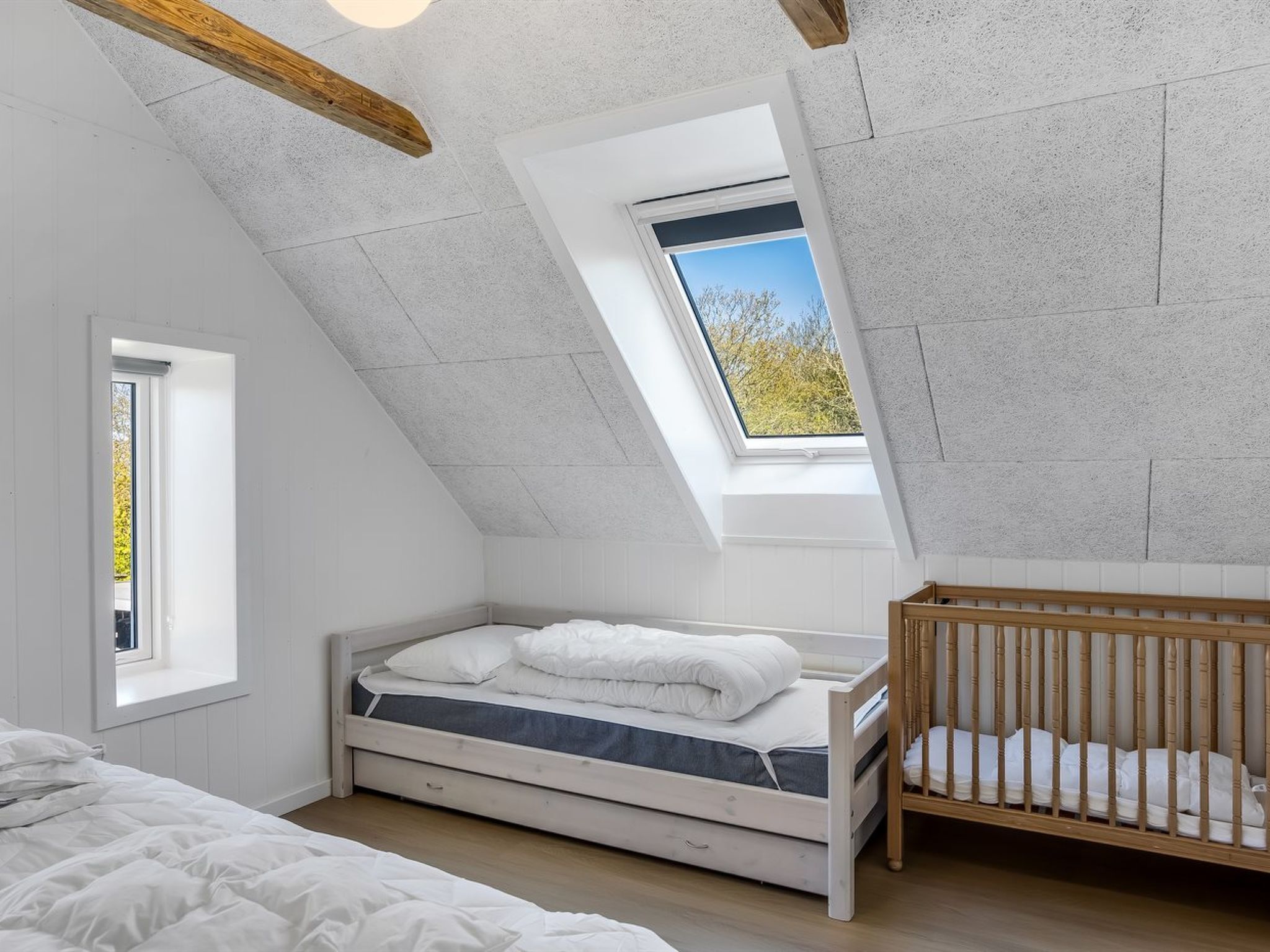 A room with a sloped ceiling, a skylight, a bed, a crib, and a window.