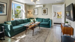 Una sala de estar con un sofá modular, una mesa de centro, un televisor y una puerta que da al exterior.