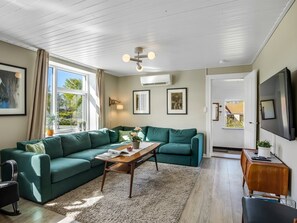 Ein Wohnzimmer mit einer Eckcouch, einem Couchtisch, einem Fernseher und einer zur Außenseite führenden Tür.