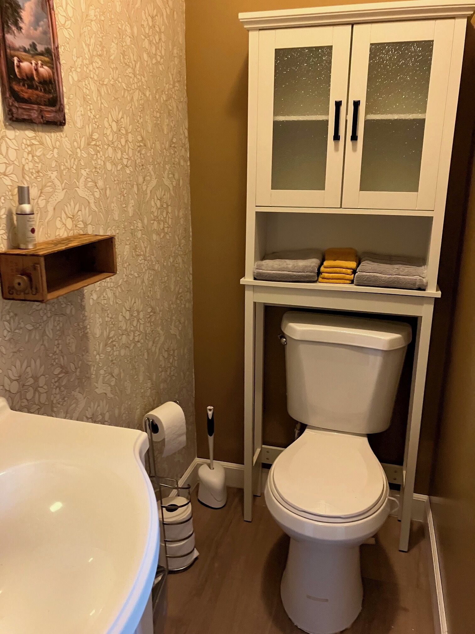 A bathroom with a toilet, a sink, a cabinet with glass doors, and a shower area.
