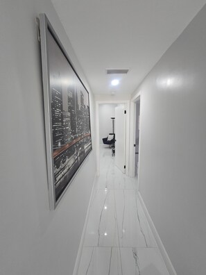 A hallway with a cityscape poster, white walls, and a shiny tiled floor.
